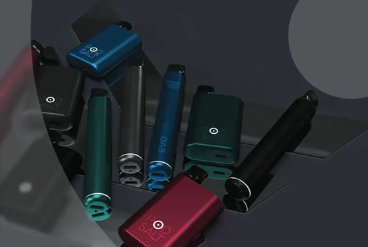 Assorted colored vape kits and disposable vape pens on dark reflective surface