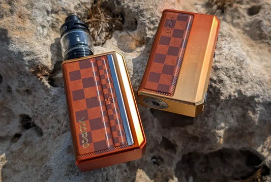 Two Voopoo vape kits with orange checkered designs placed on a rocky surface.